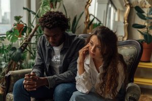 Husband sitting silently with his hands clasped while his wife looks away, both worn out after another conversation that went nowhere.